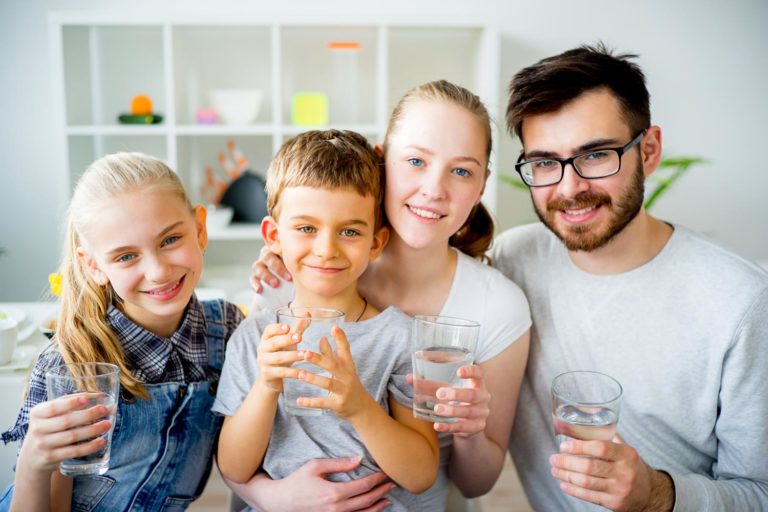 four members of a family sit together while smiling and holding clear glasses of water