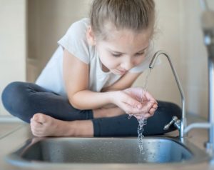 girl sitting on kitchen counter drinking water with hands from sink